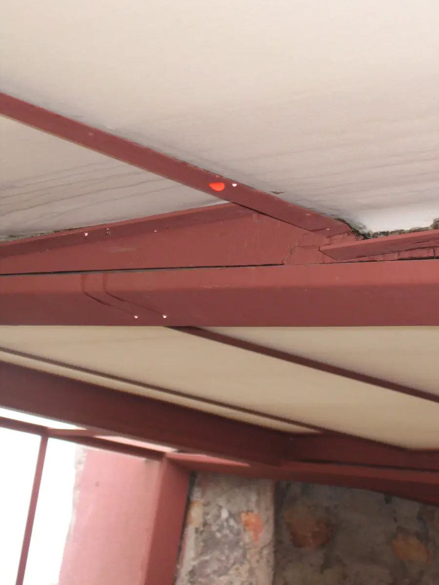 Water dripping from a leaking roof along a red steel ceiling beam