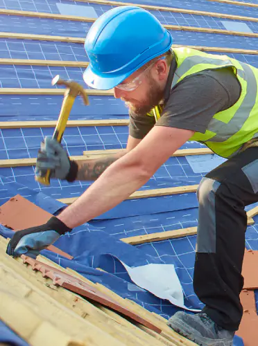 Roofer in a blue hard hat hammering battens on a pitched tile roof