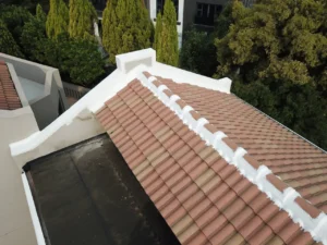 White waterproofing membrane along the ridge of a tiled roof beside a flat roof section