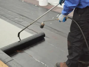 Worker torching a roll of bitumen waterproofing membrane onto a flat roof