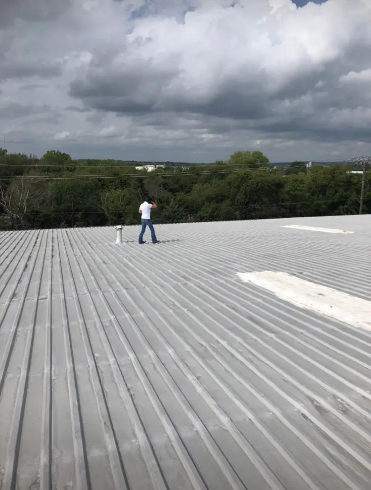 Worker standing on a large silver-coated corrugated metal roof under cloudy skies